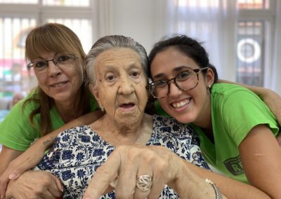 Imagen de señora mayor abrazada por dos trabajadoras de Torres Serrano apuntando a la webcam.