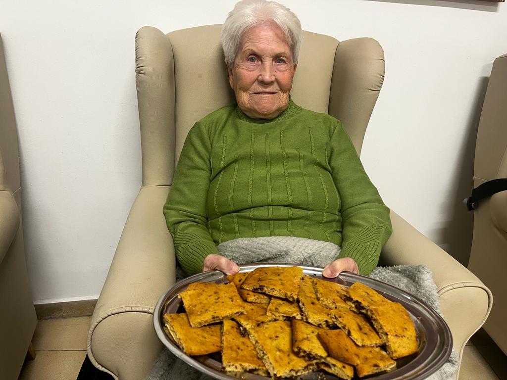 Persona mayor sentado en un sofá con una bandeja de empanadas